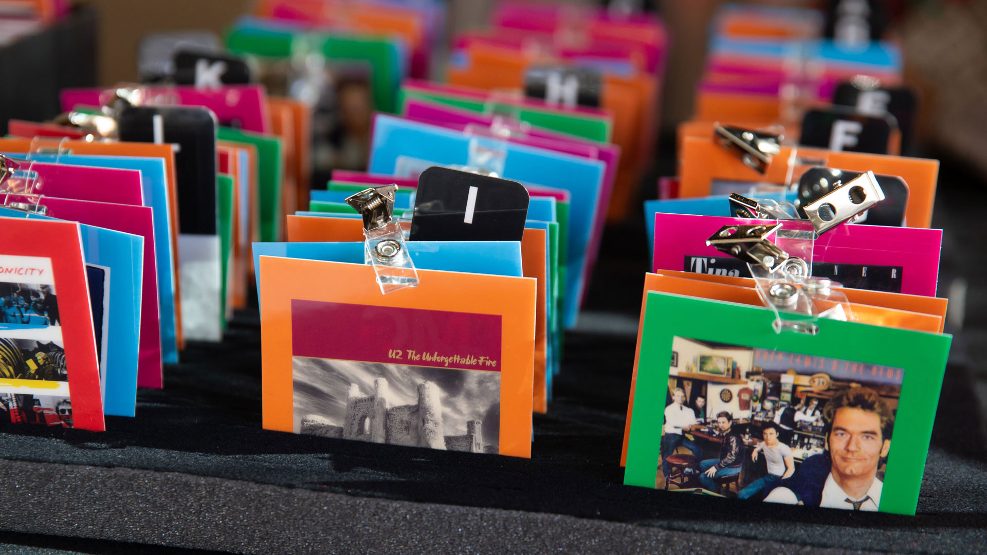 Reverse angle of name tags showing colorful back panels with 1980s album cover artwork